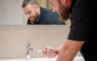 Un plombier de chez Heat Me répare un robinet dans une salle de bain