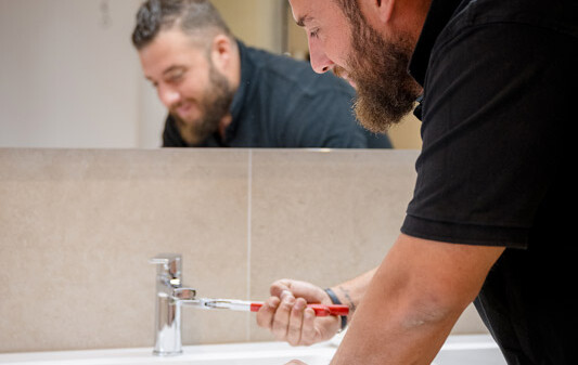 Un plombier de chez Heat Me répare un robinet dans une salle de bain