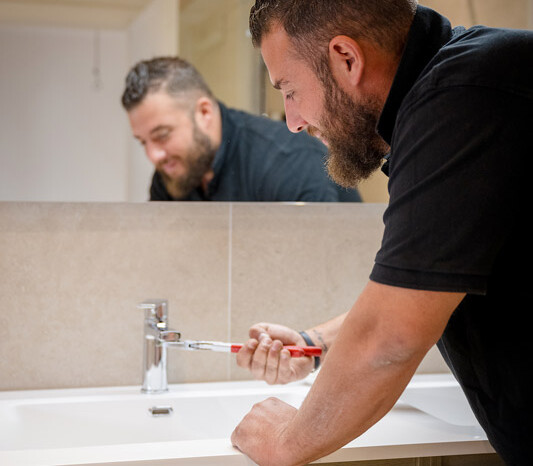 Un plombier de chez Heat Me répare un robinet dans une salle de bain